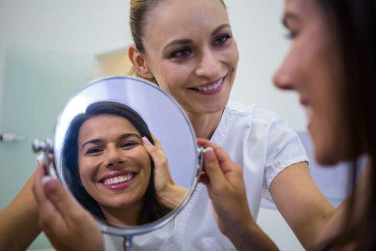 Paciente sonriente mirándose en un espejo junto a la dentista