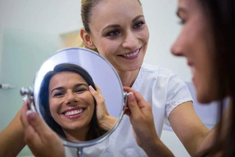 Paciente sonriente mirándose en un espejo junto a la dentista