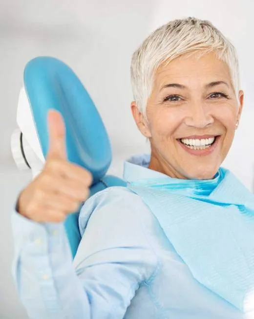 Paciente mayor sonriente con el pulgar hacia arriba en el sillón dental